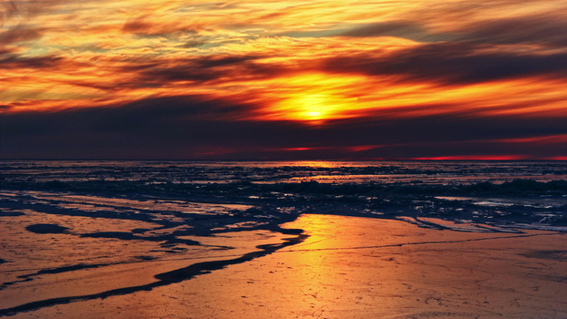 Aerial view of a vibrant sunset over a frozen landscape with glowing orange and red clouds reflecting on the icy surface in Latvia. Aerial view of a vibrant sunset over a frozen landscape with glowing orange and red clouds reflecting on the icy surface in Latvia.