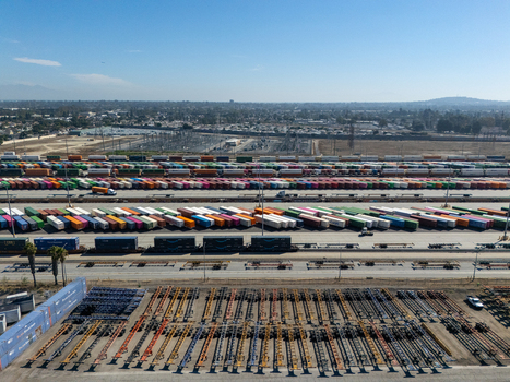 Aerial view of a large intermodal railyard filled with rows of colorful shipping containers freight trains and chassis trailers in Carson California United States.