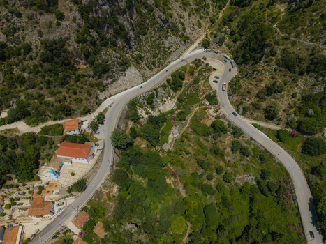 Aerial view of a winding mountain road passing by a church with a red roof and lush green hills in Dhermi Vlore County Albania. Aerial view of a winding mountain road passing by a church with a red roof and lush green hills in Dhermi Vlore County Albania.