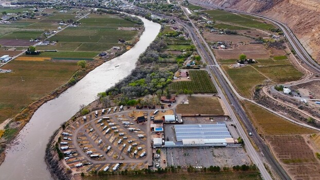 Aerial view of the winding river contrasting against the rural buildings and verdant fields nestled beneath the towering cliffs Palisade Colorado USA. Aerial view of the winding river contrasting against the rural buildings and verdant fields nestled beneath the towering cliffs Palisade Colorado USA.