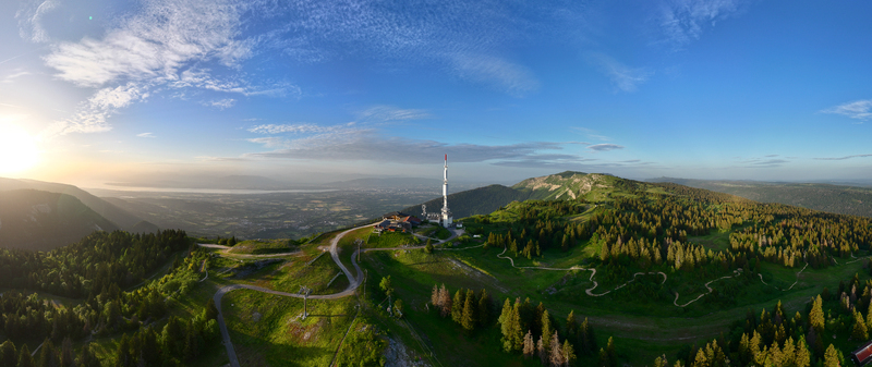 Aerial view of the Col de la Faucille mountain pass with a communication tower winding roads and dense forests overlooking a valley at sunset in Gex Auvergne Rhone Alpes France.