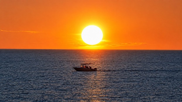 Aerial view of a small boat cruising on the calm sea during a vibrant golden sunset in Manado North Sulawesi Indonesia.