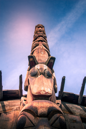View of Ksan totem pole carved from wood with intricate animal figures against a clear blue sky in Ksan British Columbia Canada. View of Ksan totem pole carved from wood with intricate animal figures against a clear blue sky in Ksan British Columbia Canada.