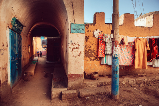 View of a narrow alleyway with an arched passage laundry hanging on a line and textured walls under warm sunlight in Aswan Aswan Governorate Egypt. View of a narrow alleyway with an arched passage laundry hanging on a line and textured walls under warm sunlight in Aswan Aswan Governorate Egypt.