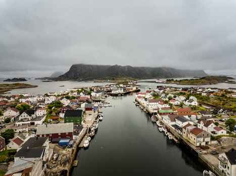 Aerial view of the fishing village of Henningsvaer with colorful houses boats docked in the harbor and dramatic mountains under a cloudy sky in Henningsvaer Nordland Norway. Aerial view of the fishing village of Henningsvaer with colorful houses boats docked in the harbor and dramatic mountains under a cloudy sky in Henningsvaer Nordland Norway.