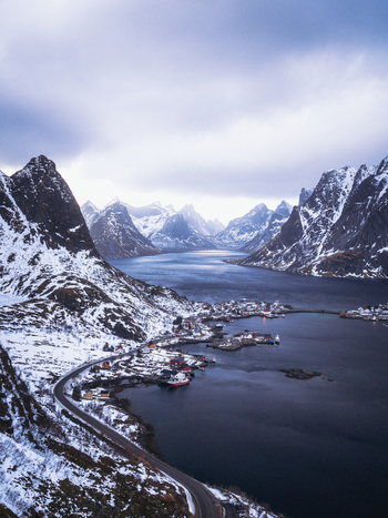 Aerial view of jagged snow dusted peaks meet the dark tranquil waters surrounding Reinebringen Nordland Norway.