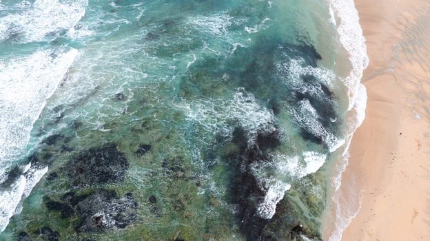 Aerial view of turquoise waves crashing against dark rocks and golden sand at Constantine Bay in Padstow Cornwall United Kingdom. Aerial view of turquoise waves crashing against dark rocks and golden sand at Constantine Bay in Padstow Cornwall United Kingdom.
