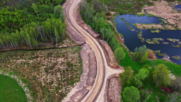 Aerial view of a dirt access road winding through a rural landscape with lush green trees and a small pond in Latvija. Aerial view of a dirt access road winding through a rural landscape with lush green trees and a small pond in Latvija.