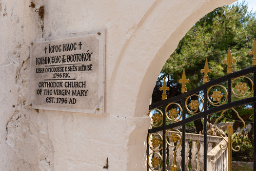 View of the entrance plaque of the Orthodox Church of the Virgin Mary with a decorative iron gate and white stone archway in Qeparo Fshat Vlore County Albania. View of the entrance plaque of the Orthodox Church of the Virgin Mary with a decorative iron gate and white stone archway in Qeparo Fshat Vlore County Albania.