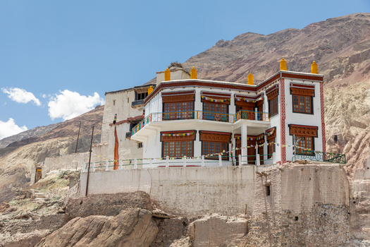 View of Charasa Gonpa a traditional white monastery with wooden windows and colorful prayer flags situated on a rocky outcrop against a mountain backdrop in Charasa Ladakh India.