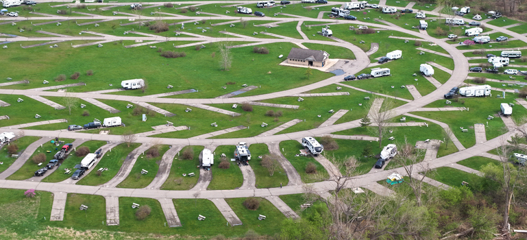 Aerial view of a spacious campground featuring numerous recreational vehicles parked on paved pads surrounded by lush green grass and trees in Monroe Michigan United States.