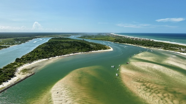 Aerial view of Matanzas Inlet featuring turquoise waters sandbars lush coastal vegetation and small boats navigating the channel in St. Johns County Florida United States. Aerial view of Matanzas Inlet featuring turquoise waters sandbars lush coastal vegetation and small boats navigating the channel in St. Johns County Florida United States.