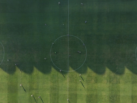 Aerial view of Maguwoharjo Stadium featuring a soccer field with players on the green grass and long shadows in Kecamatan Depok Daerah Istimewa Yogya Indonesia.