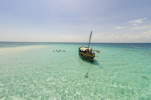 Aerial view of a traditional dhow boat and people swimming in the turquoise waters of Kisite Mpunguti Marine National Park in Kwale Kwale County Kenya. Aerial view of a traditional dhow boat and people swimming in the turquoise waters of Kisite Mpunguti Marine National Park in Kwale Kwale County Kenya.