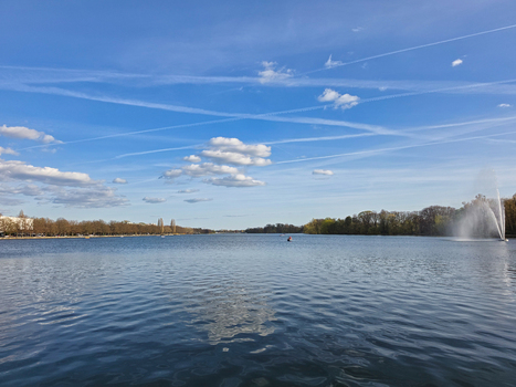 View of Maschsee lake with a fountain calm water and trees under a blue sky with contrails in Hanover Lower Saxony Germany.