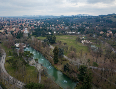 Aerial view of Giardini Margherita park featuring a long pond with fountains lush green lawns and surrounding trees under an overcast sky in Bologna Emilia Romagna Italy. Aerial view of Giardini Margherita park featuring a long pond with fountains lush green lawns and surrounding trees under an overcast sky in Bologna Emilia Romagna Italy.