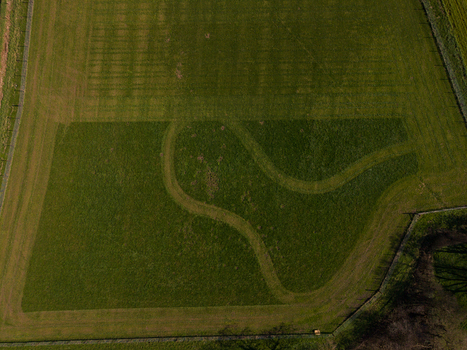 Aerial view of Gnosall Heath featuring intricate mown patterns in a lush green field surrounded by fences in Gnosall England United Kingdom. Aerial view of Gnosall Heath featuring intricate mown patterns in a lush green field surrounded by fences in Gnosall England United Kingdom.