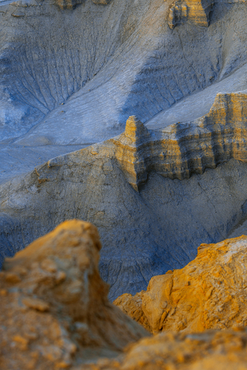 Aerial view of the rugged badlands landscape featuring dramatic geological formations eroded sandstone cliffs and contrasting golden and blue toned rock layers Hanksville Utah United States.