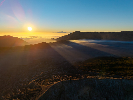 Aerial view of Mount Bromo at sunrise with golden light casting long shadows over the volcanic caldera and mist in Tosari East Java Indonesia.
