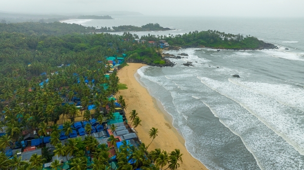 Aerial view of Palolem Beach with its golden sands dense palm groves and rows of blue roofed beach huts along the coastline in Canacona Goa India.