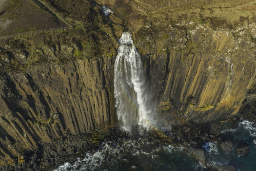 Aerial view of Kilt Rock and Mealt Falls cascading down basalt columns into the sea with waves crashing against the rocky shore Isle of Skye Scotland United Kingdom. Aerial view of Kilt Rock and Mealt Falls cascading down basalt columns into the sea with waves crashing against the rocky shore Isle of Skye Scotland United Kingdom.