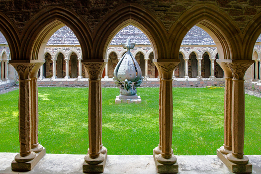 View of the cloisters of Iona Abbey and Nunnery featuring stone arches and a central sculpture in a green courtyard Isle of Iona Scotland United Kingdom. View of the cloisters of Iona Abbey and Nunnery featuring stone arches and a central sculpture in a green courtyard Isle of Iona Scotland United Kingdom.