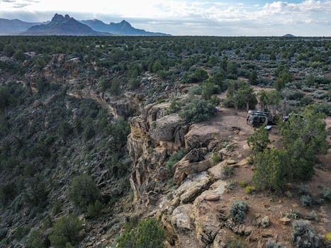 Aerial view of an overland teardrop camper trailer on the cliff edge of Gooseberry Mesa surrounded by juniper trees overlooking Zion National Park in Hurricane Utah United States.