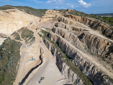 Aerial view of an open pit stone quarry with terraced rock faces dirt access roads and heavy machinery on the quarry floor in Teulada Valencian Community Spain.