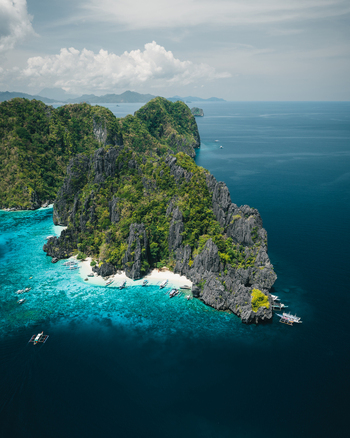 Aerial view of limestone cliffs and turquoise waters with traditional outrigger boats anchored near the white sand beach in El Nido Mimaropa Philippines. Aerial view of limestone cliffs and turquoise waters with traditional outrigger boats anchored near the white sand beach in El Nido Mimaropa Philippines.