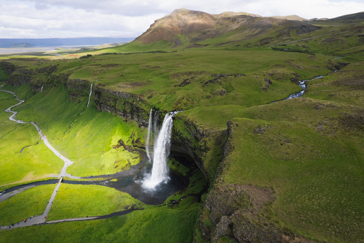 Aerial view of Seljalandsfoss waterfall cascading over a cliff into a pool surrounded by lush green hills and walking paths Rangarthing eystra Iceland. Aerial view of Seljalandsfoss waterfall cascading over a cliff into a pool surrounded by lush green hills and walking paths Rangarthing eystra Iceland.