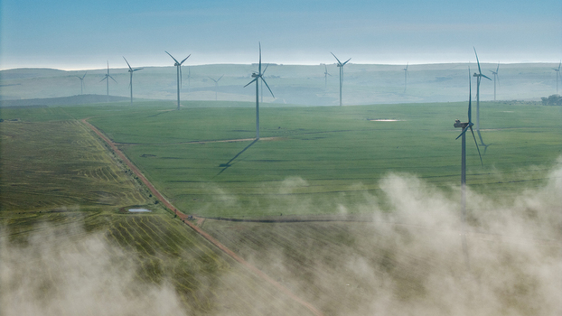 Aerial view of wind turbines in a green field with low lying mist and dirt roads in Vredenburg Western Cape South Africa. Aerial view of wind turbines in a green field with low lying mist and dirt roads in Vredenburg Western Cape South Africa.