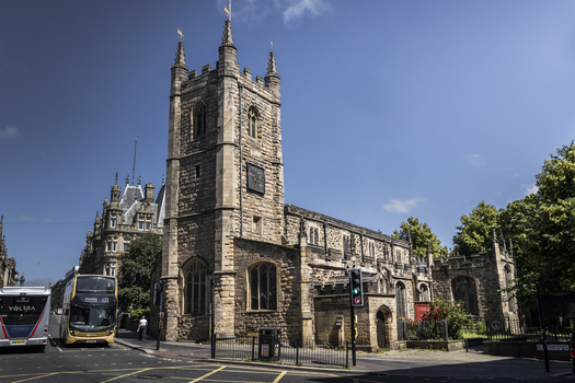 View of St John the Baptist Church with its historic stone clock tower and gothic architecture situated on a busy street in Newcastle upon Tyne England United Kingdom. View of St John the Baptist Church with its historic stone clock tower and gothic architecture situated on a busy street in Newcastle upon Tyne England United Kingdom.