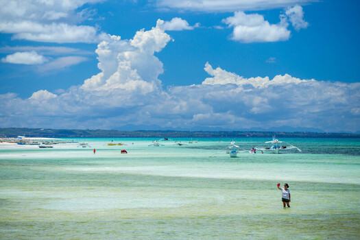 View of Bantayan Island with turquoise shallow waters traditional outrigger boats and a woman taking a selfie in the sea in Cebu Central Visayas Philippines. View of Bantayan Island with turquoise shallow waters traditional outrigger boats and a woman taking a selfie in the sea in Cebu Central Visayas Philippines.