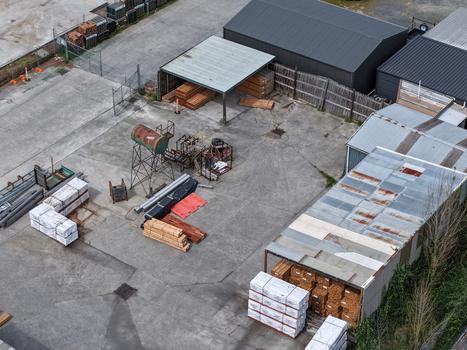 Melbourne VIC Australia 25 September 2026 Aerial view of an industrial yard featuring stacks of timber metal storage sheds and scattered machinery on a concrete surface.