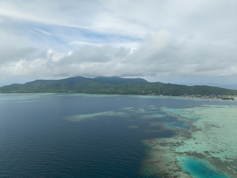Aerial view of the island s dark blue waters meeting the vibrant turquoise reef with lush green hills under a cloudy sky Karimunjawa Central Java Indonesia.