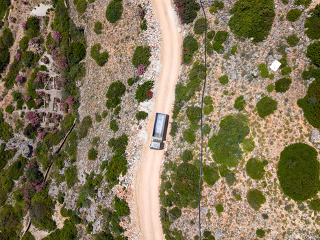 Aerial view of a truck driving on a winding dirt road through a rocky hillside with green shrubs pink flowers and ancient stone ruins in Borsh Vlore County Albania. Aerial view of a truck driving on a winding dirt road through a rocky hillside with green shrubs pink flowers and ancient stone ruins in Borsh Vlore County Albania.