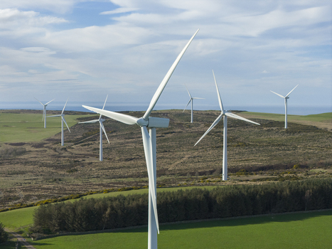 Aerial view of a windfarm with white turbines standing over green fields and moorland under a blue sky in Scotland United Kingdom. Aerial view of a windfarm with white turbines standing over green fields and moorland under a blue sky in Scotland United Kingdom.