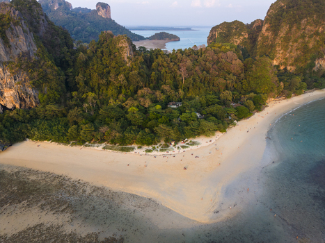 Aerial view of vibrant turquoise waters meet the soft sandy beach framed by majestic limestone cliffs cloaked in lush greenery Krabi Thailand.
