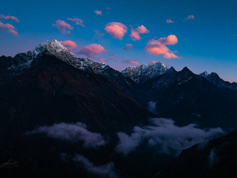 Aerial view of the snow capped Himalayan peaks illuminated by the soft pink glow of sunset with low lying clouds drifting through the deep mountain valleys in Nepal.