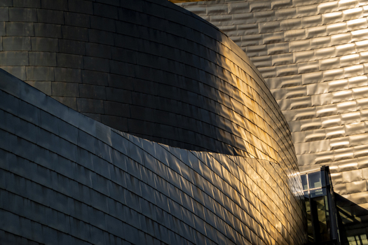 View of the curved titanium panels of the Guggenheim Museum Bilbao reflecting warm golden sunlight on the architectural facade in Bilbao Euskadi Spain. View of the curved titanium panels of the Guggenheim Museum Bilbao reflecting warm golden sunlight on the architectural facade in Bilbao Euskadi Spain.