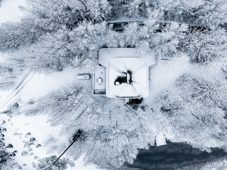 Aerial view of a house surrounded by snow covered trees and a small pond in Latvia. Aerial view of a house surrounded by snow covered trees and a small pond in Latvia.
