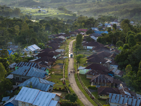 Aerial view of Bangka Kenda village with houses featuring metal roofs along a central road surrounded by lush hills and greenery in Wae Rii East Nusa Tenggara Indonesia.
