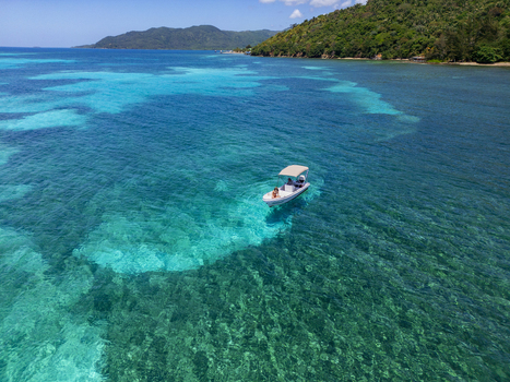 Aerial view of a small boat floating on crystal clear turquoise waters near the lush green coastline of Guanaja Bay Islands Department Honduras. Aerial view of a small boat floating on crystal clear turquoise waters near the lush green coastline of Guanaja Bay Islands Department Honduras.