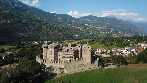 Aerial view of the medieval Fenis Castle with its stone towers and crenelated walls nestled in a lush green valley surrounded by the Alps in Aosta Valley Aosta Valley Italy. Aerial view of the medieval Fenis Castle with its stone towers and crenelated walls nestled in a lush green valley surrounded by the Alps in Aosta Valley Aosta Valley Italy.