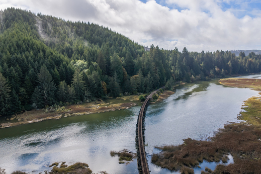 Aerial view of the Coos Bay Rail Line curving across wetlands beside the Siuslaw River near Florence Oregon with coastal rail infrastructure surrounded by forest and tidal marsh.