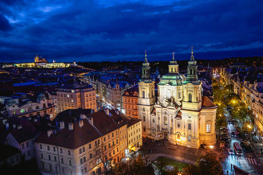 Aerial view of St. Nicholas Church illuminated at night with Prague Castle in the distance surrounded by historic buildings and city lights in Prague Prague Czechia. Aerial view of St. Nicholas Church illuminated at night with Prague Castle in the distance surrounded by historic buildings and city lights in Prague Prague Czechia.