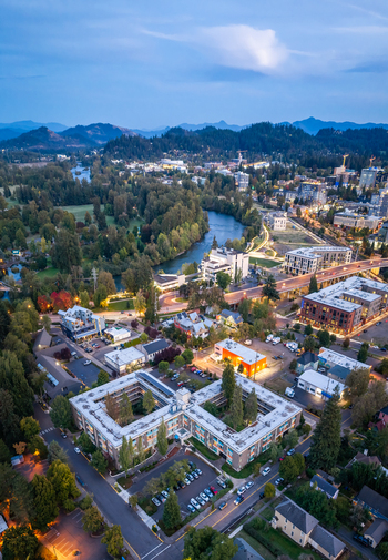 Aerial view of Eugene s Downtown Riverfront Park beside the Willamette River surrounded by trees residential buildings and city lights at dusk. Aerial view of Eugene s Downtown Riverfront Park beside the Willamette River surrounded by trees residential buildings and city lights at dusk.