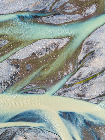 Aerial view of a braided glacial river with turquoise sediment rich water flowing through dark volcanic gravel bars in Iceland. Aerial view of a braided glacial river with turquoise sediment rich water flowing through dark volcanic gravel bars in Iceland.