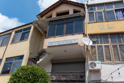 View of a multi story building featuring an internet cafe sign satellite dish and air conditioning unit under a blue sky in Kruje Durres County Albania.
