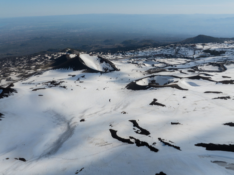 Aerial view of the snow covered volcanic craters on the south slope of Mount Etna with dark lava rock under a clear blue sky in Nicolosi Sicilia Italy. Aerial view of the snow covered volcanic craters on the south slope of Mount Etna with dark lava rock under a clear blue sky in Nicolosi Sicilia Italy.